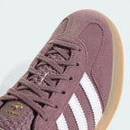 Close-up of the tongue, highlighting the gold Trefoil logo and the fine texture of the plum suede.