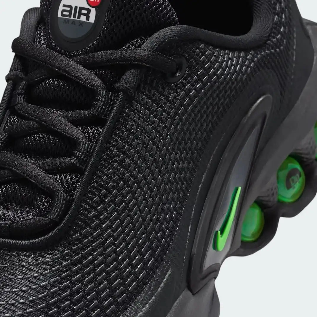 Close-up zoom on the front of the Nike Air Max DN Juniors' black running trainers, showing the mesh upper texture, haptic print details, and lacing system.