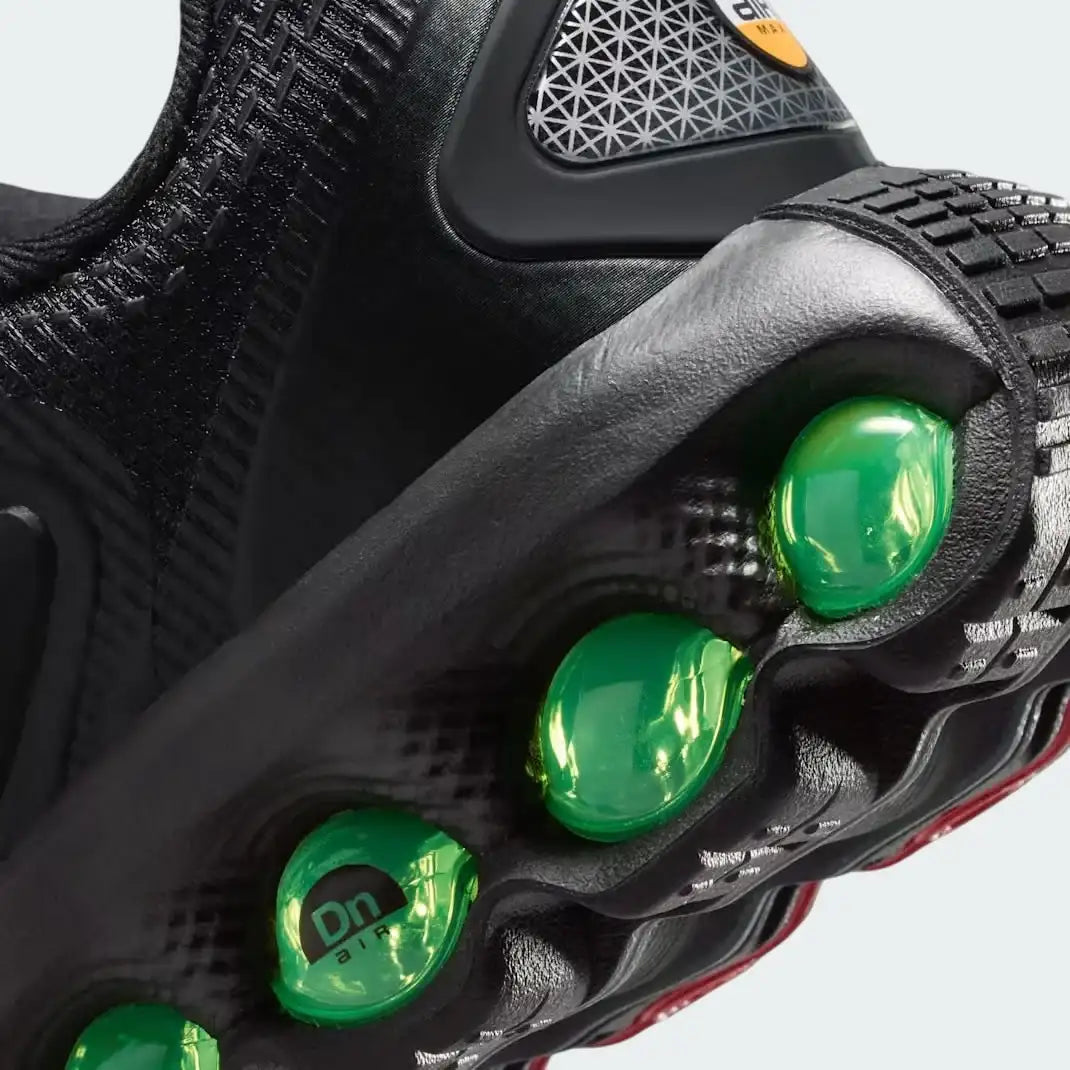 Detailed zoom on the outsole and midsole of the Nike Air Max DN Juniors' black running trainers, highlighting the dual-pressure Dynamic Air cushioning system and robust rubber outsole.