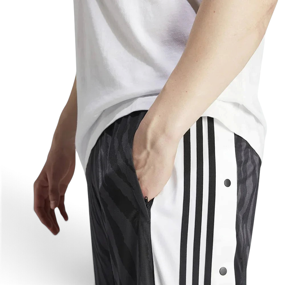Close-up zoom on the fabric of the Adidas Adibreak Track Pants, showing the smooth polyester texture, the subtle tonal animal print, and the side snap buttons.