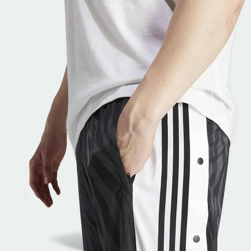 Close-up zoom on the fabric of the Adidas Adibreak Track Pants, showing the smooth polyester texture, the subtle tonal animal print, and the side snap buttons.