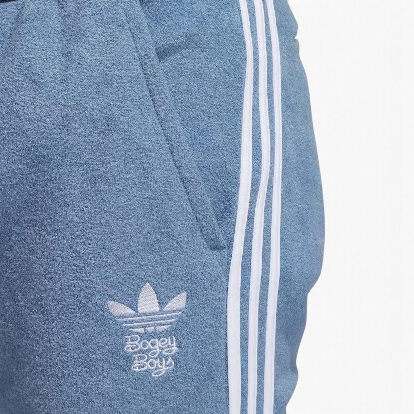 Close-up zoom on the fabric of the Adidas x Bogey Boys Golf Track Pants in blue, showing the texture and the embroidered Trefoil/Bogey Boys logo detail.