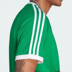 Side profile of the green Adicolor Sport t-shirt, showcasing the iconic white 3-Stripes running from the shoulder to the sleeve hem.