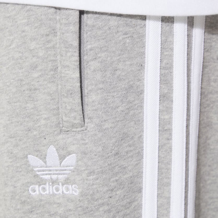 Close-up of the upper thigh area, focusing on the high-quality embroidery of the Trefoil logo and the secure zip pocket detail.