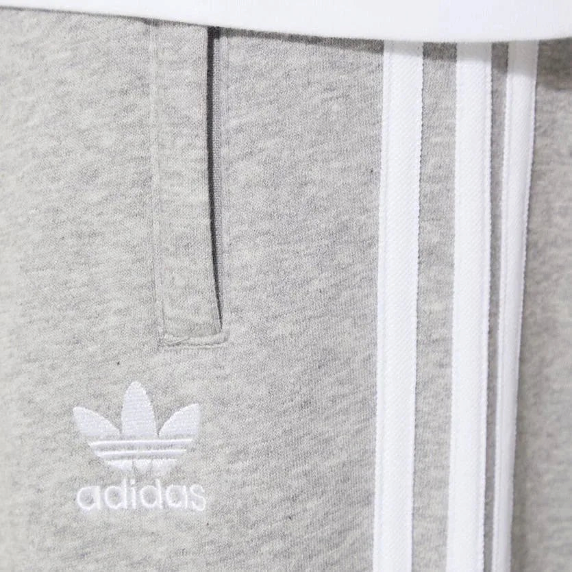 Close-up of the upper thigh area, focusing on the high-quality embroidery of the Trefoil logo and the secure zip pocket detail.