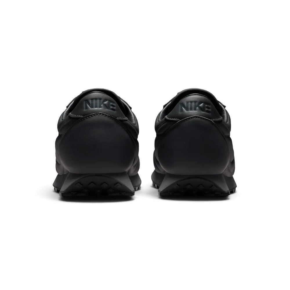 Showing the structured rear heel counter, detailing the light bone leather heel tab with vintage Nike block text, textured leather heel cup, and tapered foam wedge heel.
