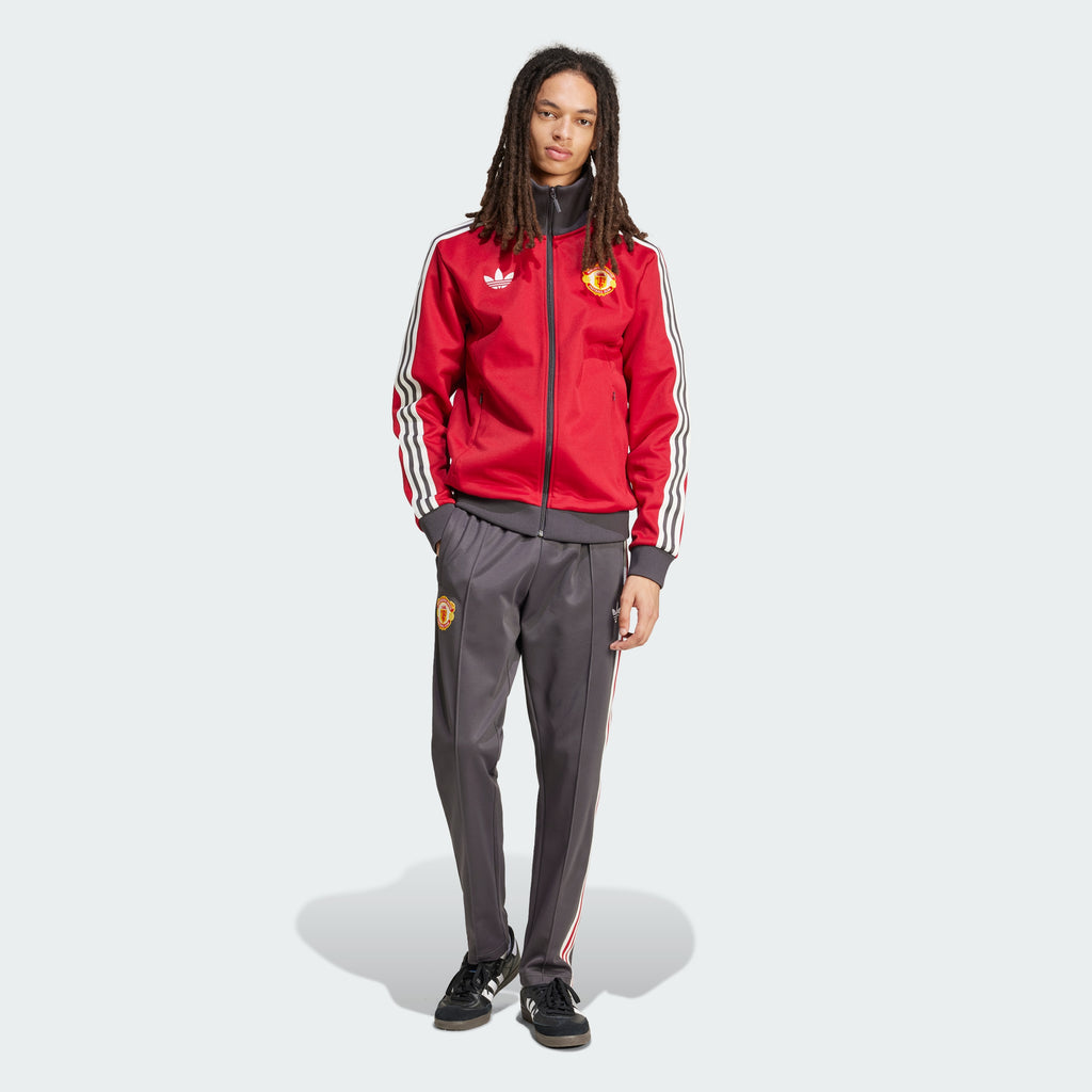 Person wearing a red tracksuit with Adidas and Manchester United logos on a white background