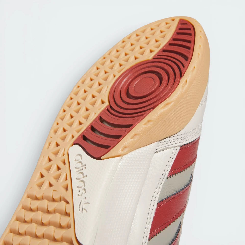 Close-up of a sneaker's sole with red and beige pattern on a light gray background