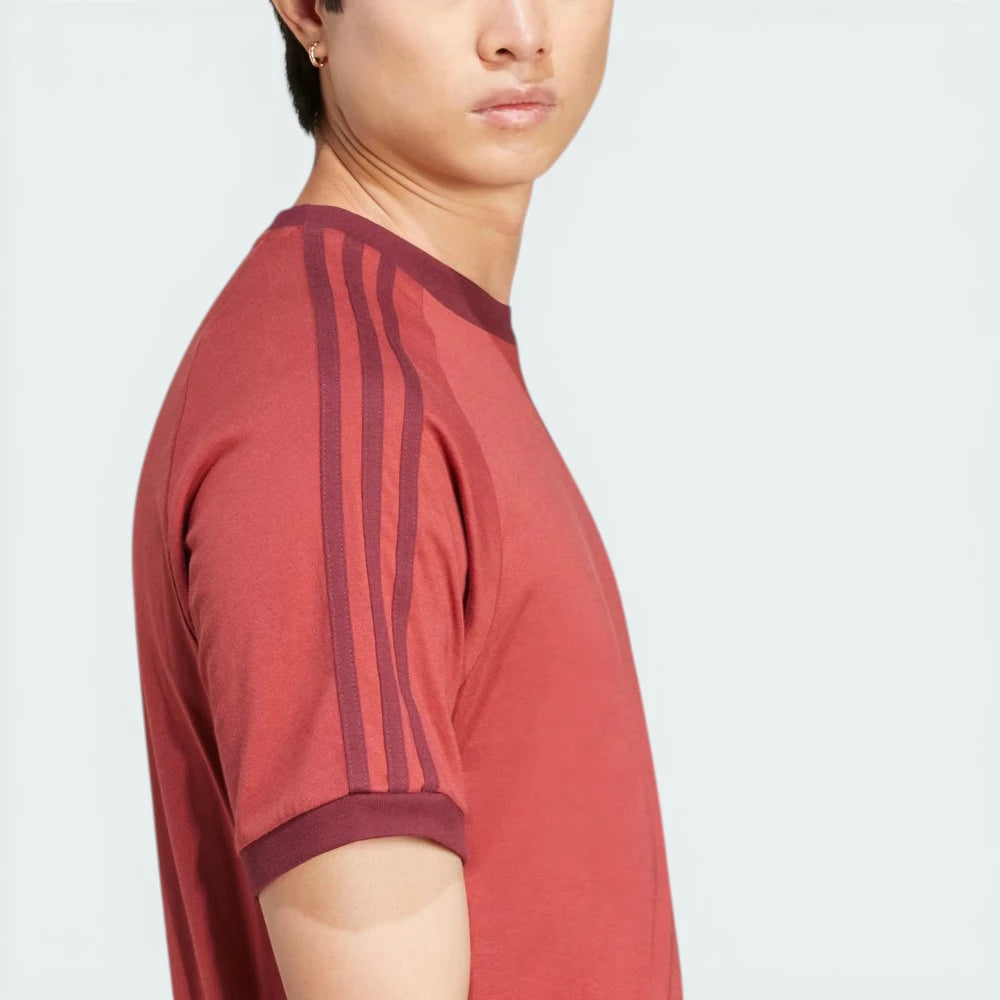Side profile of the Preloved Ruby Adidas t-shirt, showcasing the iconic white 3-Stripes running from the shoulder to the ribbed cuff.