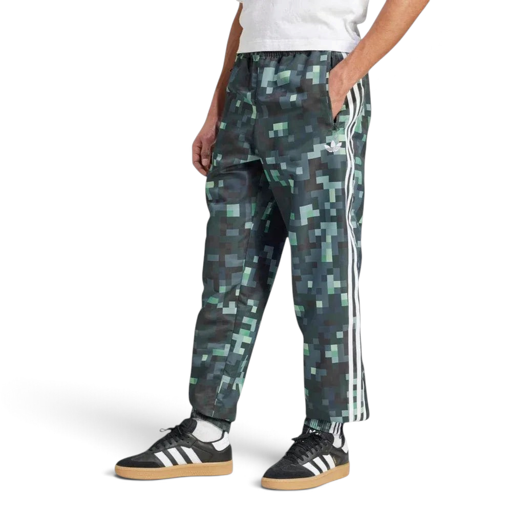 Side profile of the adidas x Minecraft track pants, showing the color gradient from light grey to dark green and the woven twill texture.