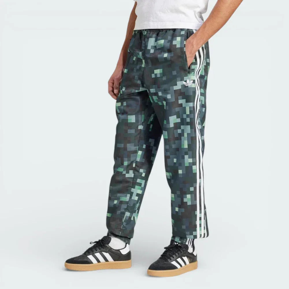 Side profile of the adidas x Minecraft track pants, showing the color gradient from light grey to dark green and the woven twill texture.