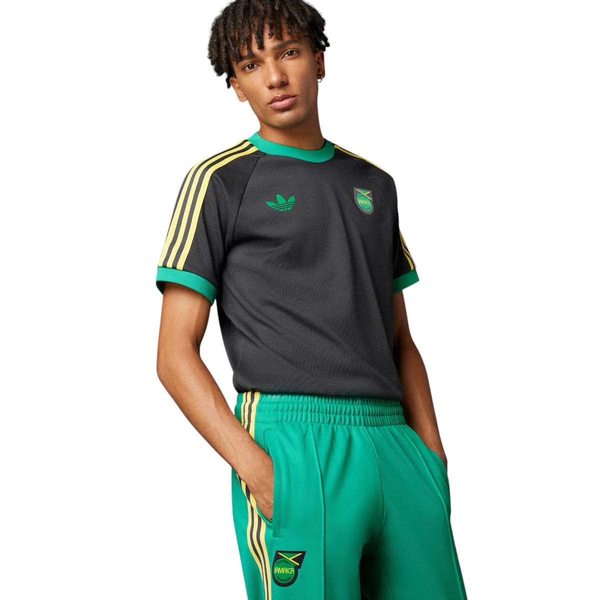 Close-up studio shot of a model posing with hands in pockets, emphasizing the structured waistline, front center stitching creases, and the Jamaica crest placement.