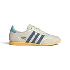Highlights the sleek, low-profile lateral view showing the off-white perforated leather upper, deep Preloved Ink navy adidas Three Stripes, double-stitched T-toe overlay, Orange Tint accent paneling, and slim rubber sole.