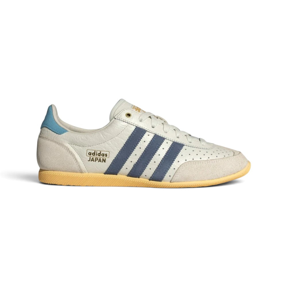 Highlights the sleek, low-profile lateral view showing the off-white perforated leather upper, deep Preloved Ink navy adidas Three Stripes, double-stitched T-toe overlay, Orange Tint accent paneling, and slim rubber sole.