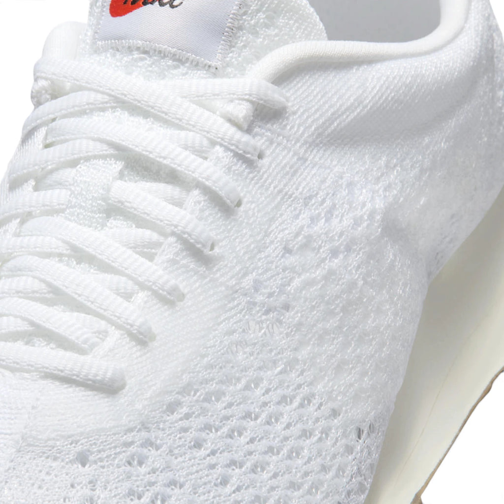 Macro focus on the forefoot and eyestay, detailing the breathable Flyknit texture, flat white laces, and orange-accented Nike tongue label.