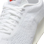 Macro focus on the forefoot and eyestay, detailing the breathable Flyknit texture, flat white laces, and orange-accented Nike tongue label.