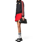 Studio full-body shot of a model wearing the track top alongside a red skirt, white socks, and black slides, demonstrating its high-fashion streetwear versatility