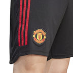 Macro close-up angle capturing the textured fabric weave, vibrant red 3-Stripes tape, and the precision embroidery of the Manchester United woven club badge.