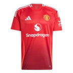 Clean studio product shot of the Manchester United 24/25 home jersey in Mufc Red, highlighting the classic crewneck, white sponsor branding, embroidered club crest, and bright red side inserts.