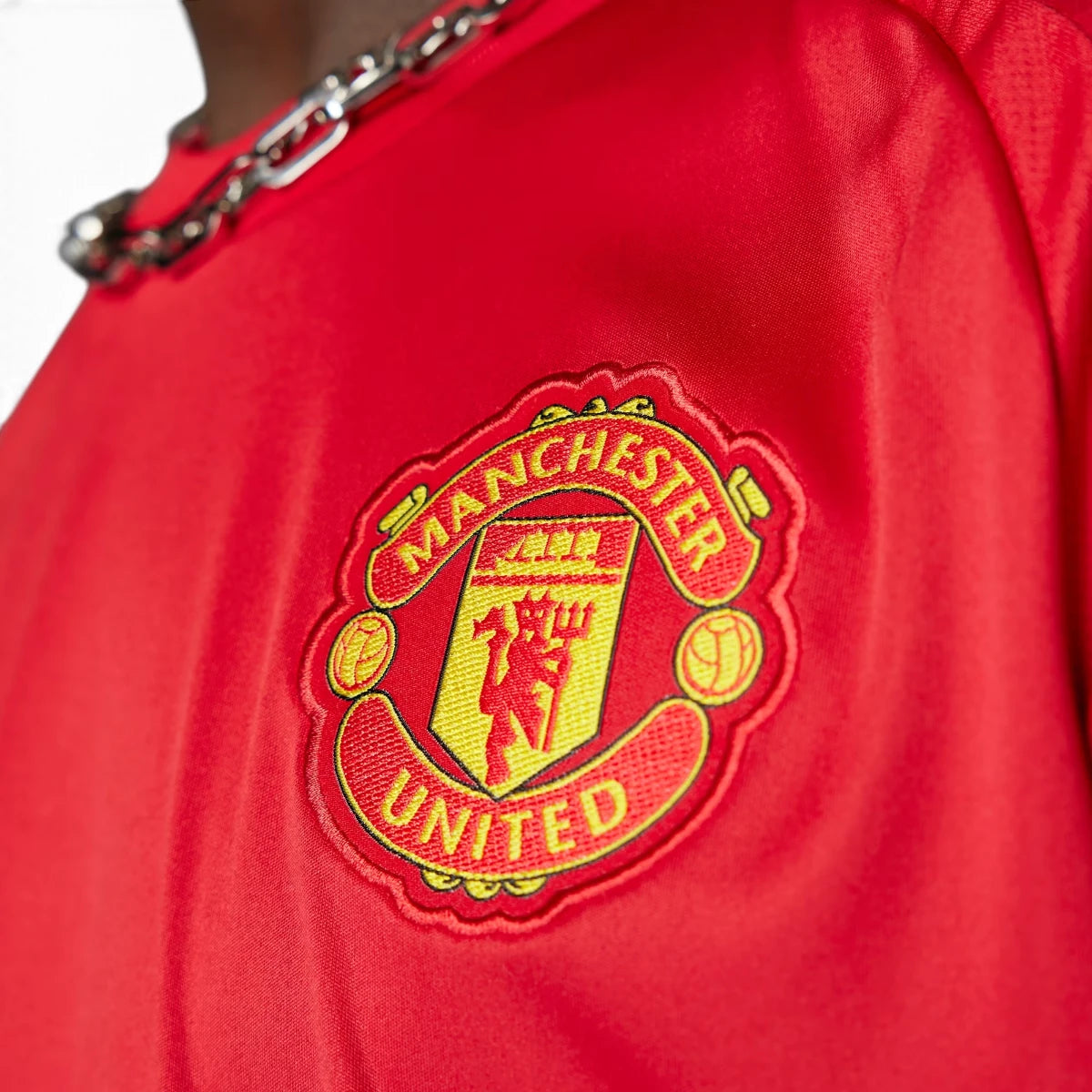 Macro close-up angle capturing the textured fabric weave, precision stitching of the embroidered Manchester United club badge, and sponsor logo details.