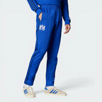 The Bold Blue track pants, highlighting the slim-cut leg and the vintage white Adidas 3-Stripes.