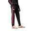Studio side profile view of a model wearing the adidas Manchester United Terrace Icons Track Pants in black, highlighting the slim fit, red-and-white 3-Stripes taping, vintage Manchester United embroidered crest, front zip pockets, and ribbed cuffs.
