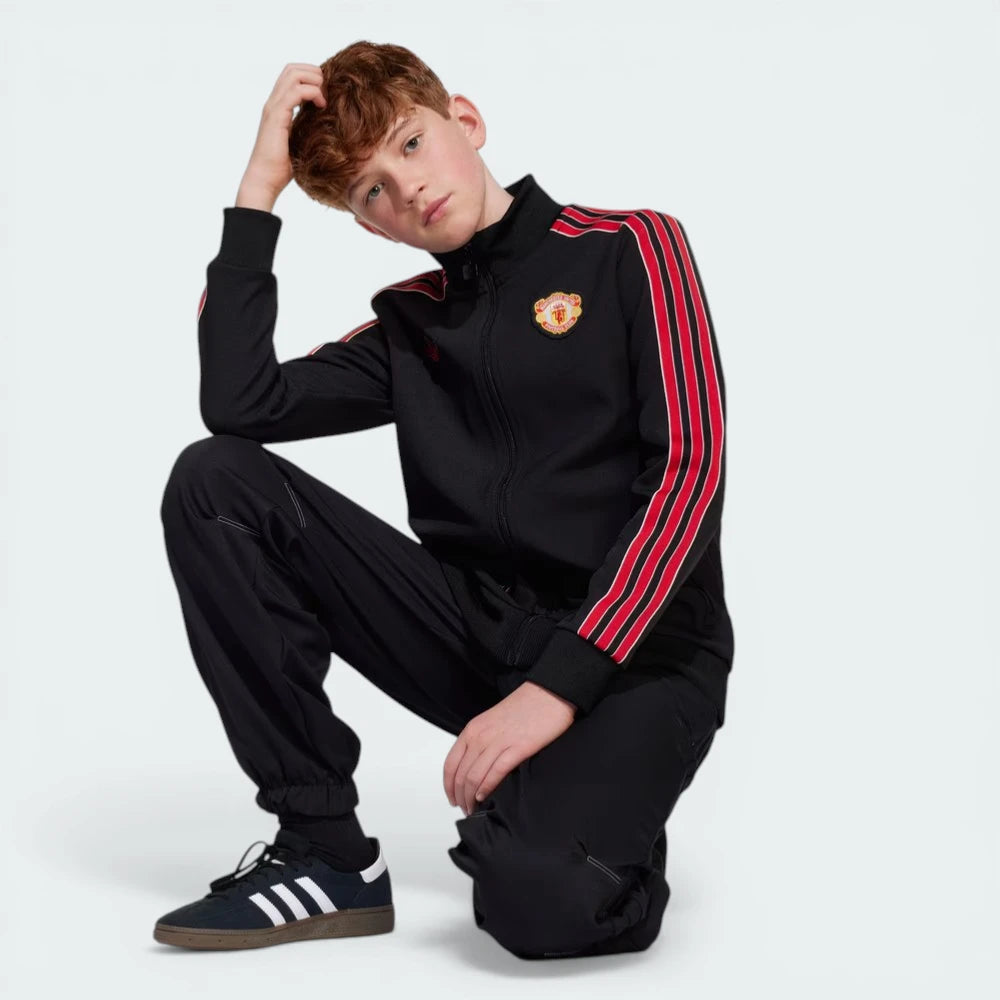 Person wearing a black tracksuit with red stripes and a logo, sitting on the ground.