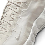 Close-up of a Nike sneaker in a monochromatic off-white color, showing the textured upper, laces, and the embossed Swoosh logo.