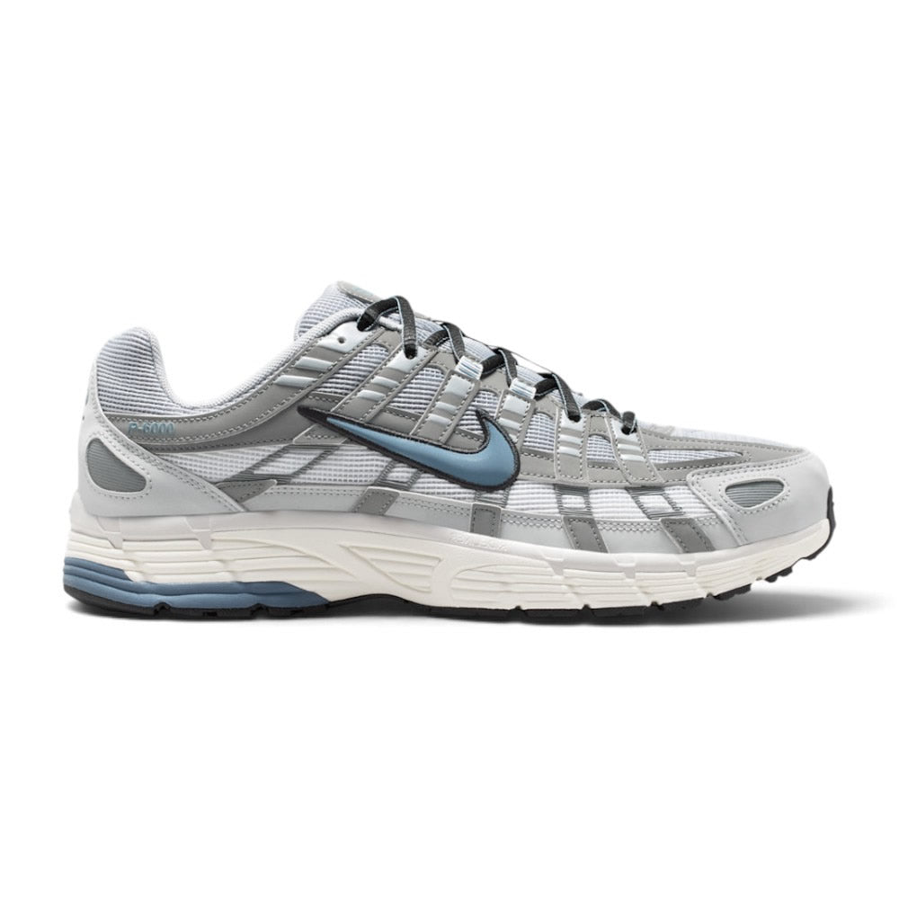 Highlights the early-2000s lateral silhouette featuring the Summit White mesh upper, layered grey and silver cross-hatch overlays, slate-blue Nike Swoosh with black embroidered trim, vintage Sail foam midsole with blue heel insert, and black rubber outsole.