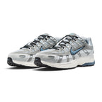 Emphasising the low-slung, technical stance of the trainers and the high-contrast harmony between the breathable white mesh base, metallic silver cage panels, and subtle blue accent hits.