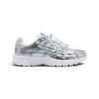 Highlights the early-2000s lateral silhouette featuring gleaming Metallic Silver horizontal and vertical overlays sweeping over white breathable mesh, a white Swoosh with silver outline, toggle lace system, and a grooved white foam sole.
