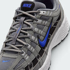 Details the micro-precision of the grey mesh toe box, showing the silver synthetic toe bumper, mini blue Swoosh, matching grey laces, and the black tongue patch printed with blue "NIKE" block lettering.