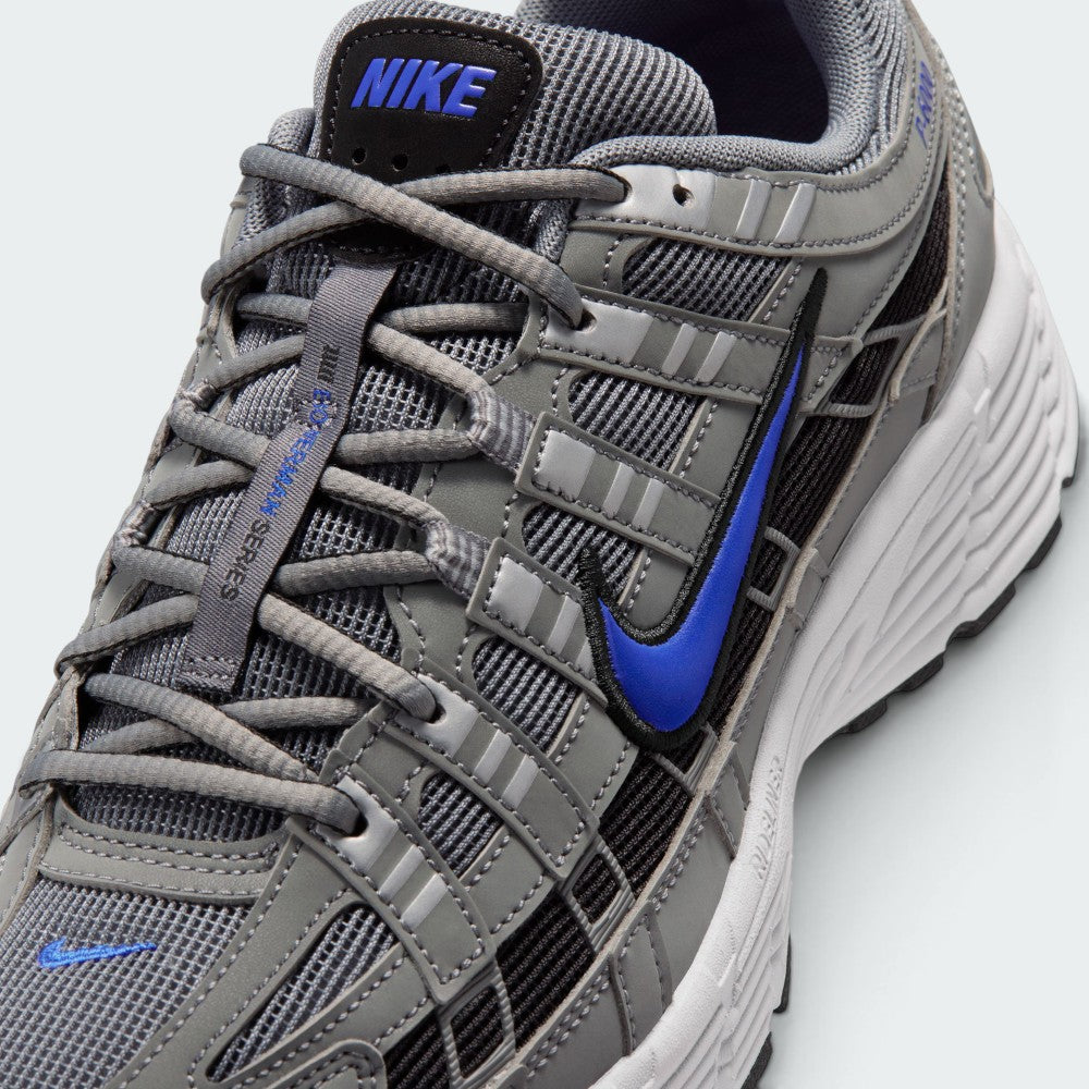 Details the micro-precision of the grey mesh toe box, showing the silver synthetic toe bumper, mini blue Swoosh, matching grey laces, and the black tongue patch printed with blue "NIKE" block lettering.