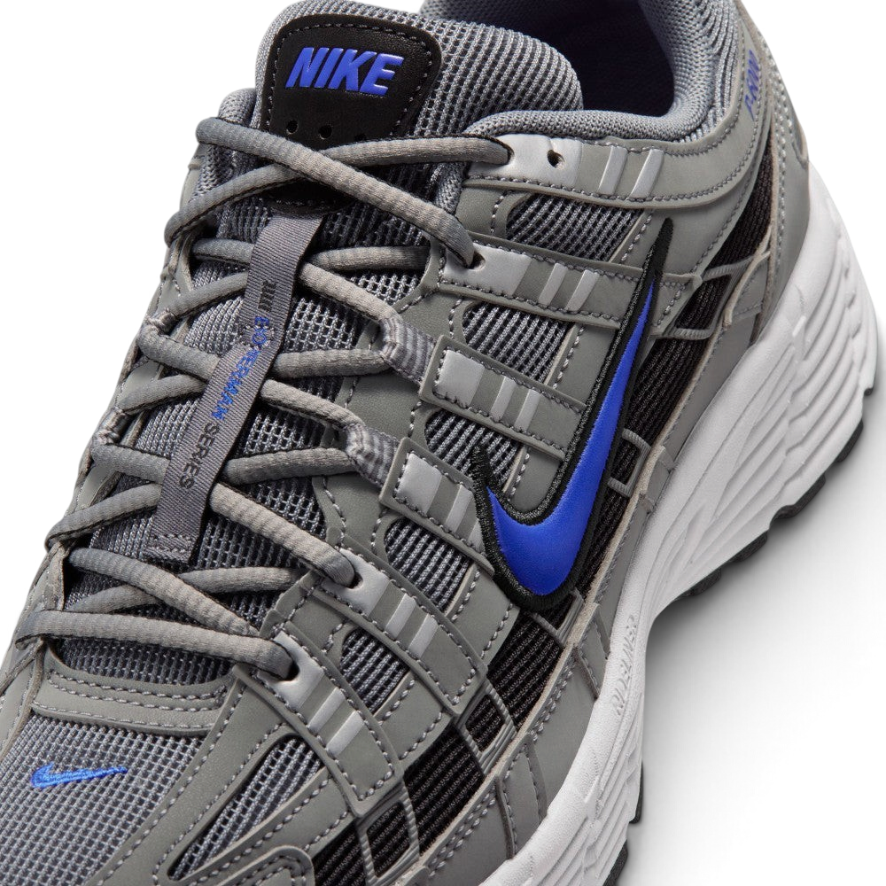 Details the micro-precision of the grey mesh toe box, showing the silver synthetic toe bumper, mini blue Swoosh, matching grey laces, and the black tongue patch printed with blue "NIKE" block lettering.