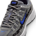 Details the micro-precision of the grey mesh toe box, showing the silver synthetic toe bumper, mini blue Swoosh, matching grey laces, and the black tongue patch printed with blue "NIKE" block lettering.