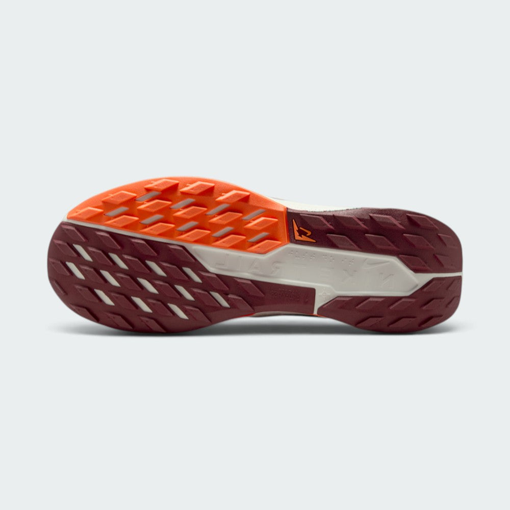 Displays the full-length Nike Trail All-Terrain Compound (ATC) rubber sole split between Dark Team Red and Hyper Crimson tread sections, showcasing the multi-directional lug grid and central Sail stability shank with trail logo.