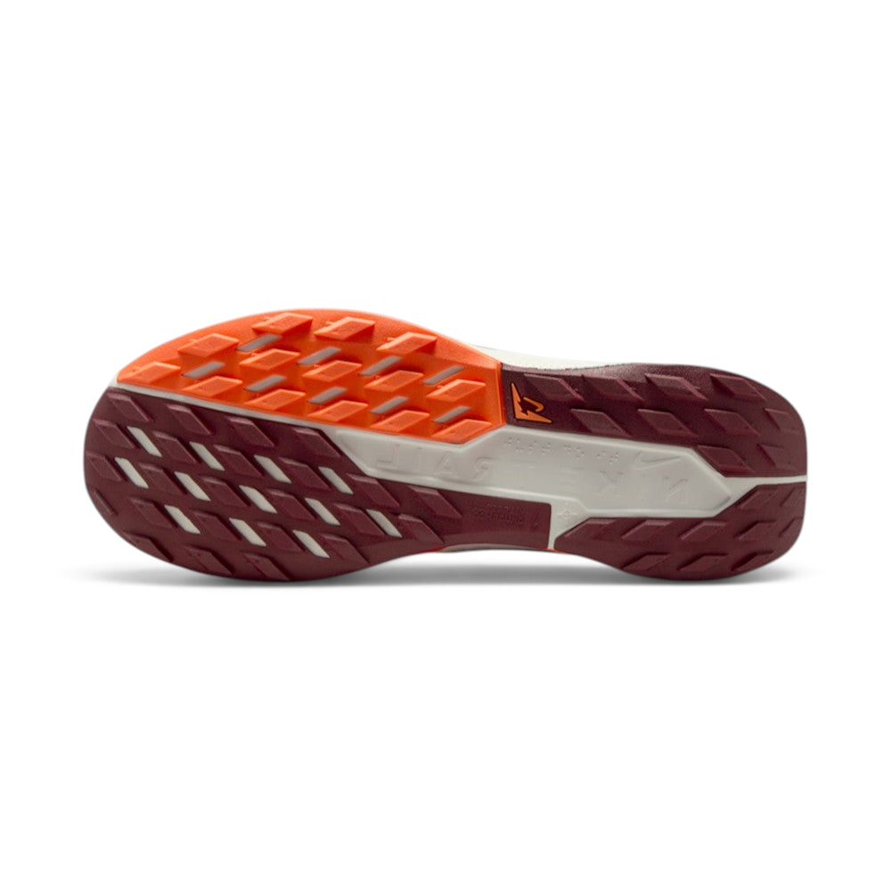 Displays the full-length Nike Trail All-Terrain Compound (ATC) rubber sole split between Dark Team Red and Hyper Crimson tread sections, showcasing the multi-directional lug grid and central Sail stability shank with trail logo.