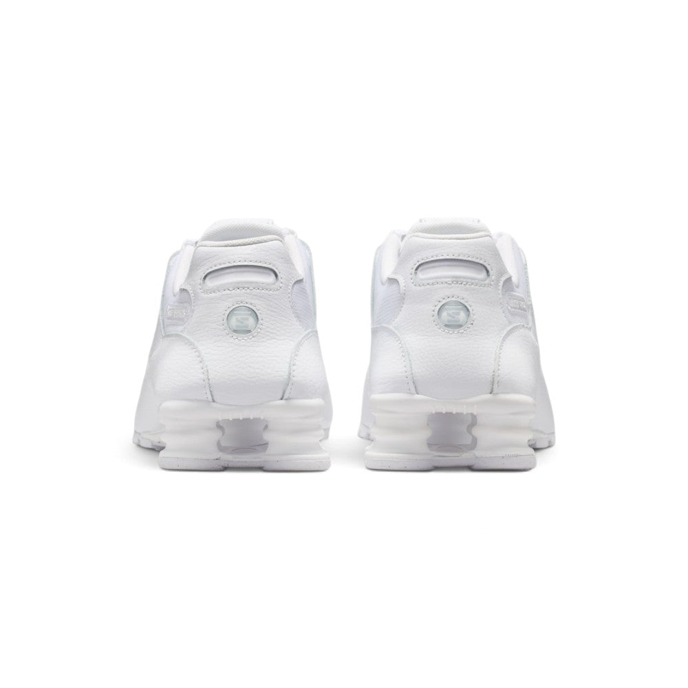Close-up rear angle focusing on the four white Nike Shox columns between dual transition plates, central heel branding window, reflective accents, and the protective rubber outsole wrap.