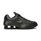 Lateral view showing the aerodynamic black synthetic casing, precision laser perforations along the midfoot, tonal Nike Swoosh badge, and the iconic four Bright Crimson Nike Shox columns compressed beneath the black TPU heel moderator plate.