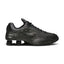 Lateral view showing the aerodynamic black synthetic casing, precision laser perforations along the midfoot, tonal Nike Swoosh badge, and the iconic four Bright Crimson Nike Shox columns compressed beneath the black TPU heel moderator plate.