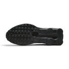 Full-length bottom profile showing the solid black rubber outsole, showcasing the modified circular Waffle traction pattern, forefoot flex grooves, and open central cavity revealing the crimson Shox column bases.