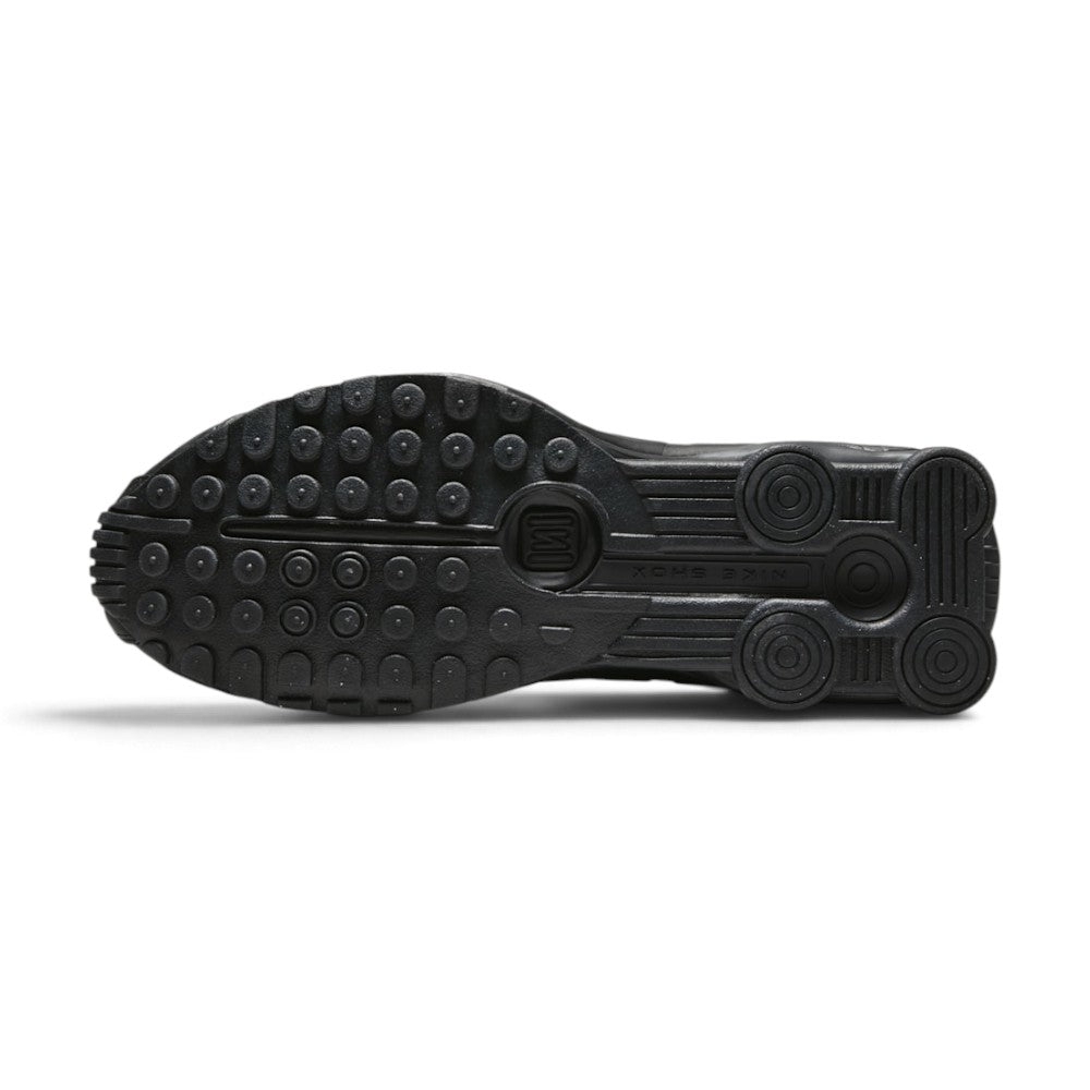 Full-length bottom profile showing the solid black rubber outsole, showcasing the modified circular Waffle traction pattern, forefoot flex grooves, and open central cavity revealing the crimson Shox column bases.