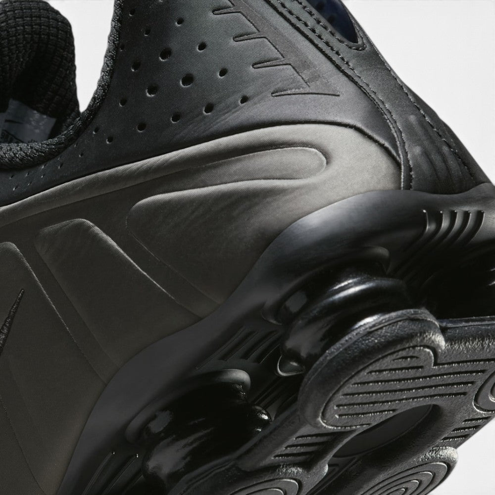 Highlights the mechanical finish where the black foam forefoot transitions into the rigid TPU heel plate, framing the Bright Crimson Shox cushioning units above the durable rubber tread.