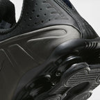Highlights the mechanical finish where the black foam forefoot transitions into the rigid TPU heel plate, framing the Bright Crimson Shox cushioning units above the durable rubber tread.