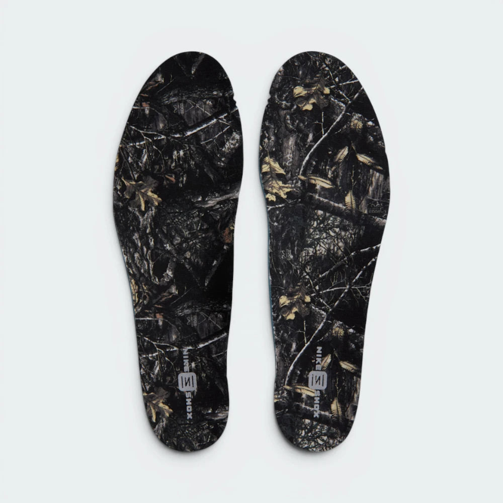 Displays the removable black insoles printed with a full RealTree woodland branch-and-leaf camouflage pattern, finished with silver "NIKE SHOX" branding at the heel.