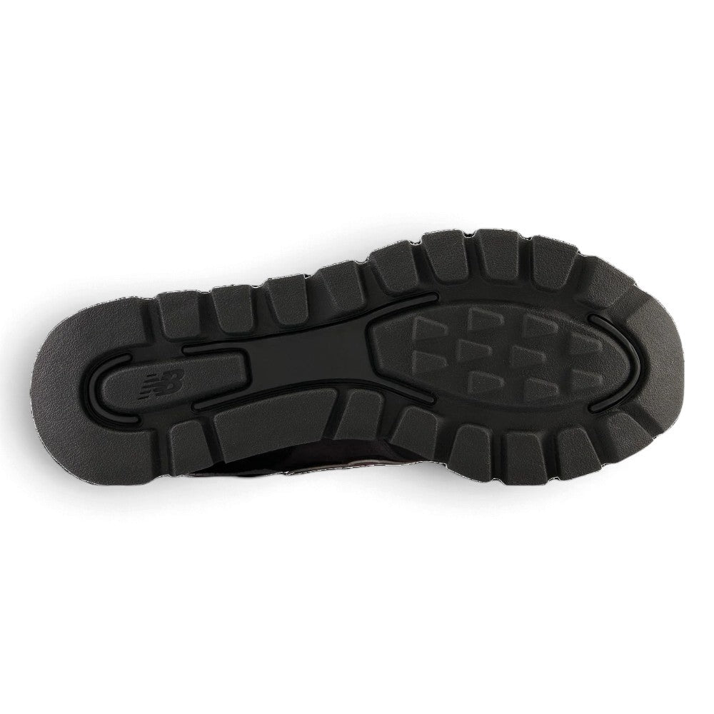 Full-length bottom profile showing the heavy-duty black rubber outsole, highlighting the pronounced trail-ready traction lugs, flex grooves for natural heel-to-toe roll, and embossed central New Balance branding.