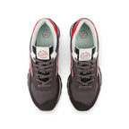 Direct overhead view of both shoes laid flat, showcasing the rounded suede toe cap, breathable mesh toe box, flat grey laces threaded through punched eyestays, padded mesh tongue with woven New Balance 574 crest patch, and cushioned interior sockliner.