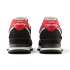 Close-up rear angle focusing on the supportive black suede heel wrap, bold red leather heel tab with white printed "new balance" typography, external TPU stabiliser clip, and flared rubber outsole rim.