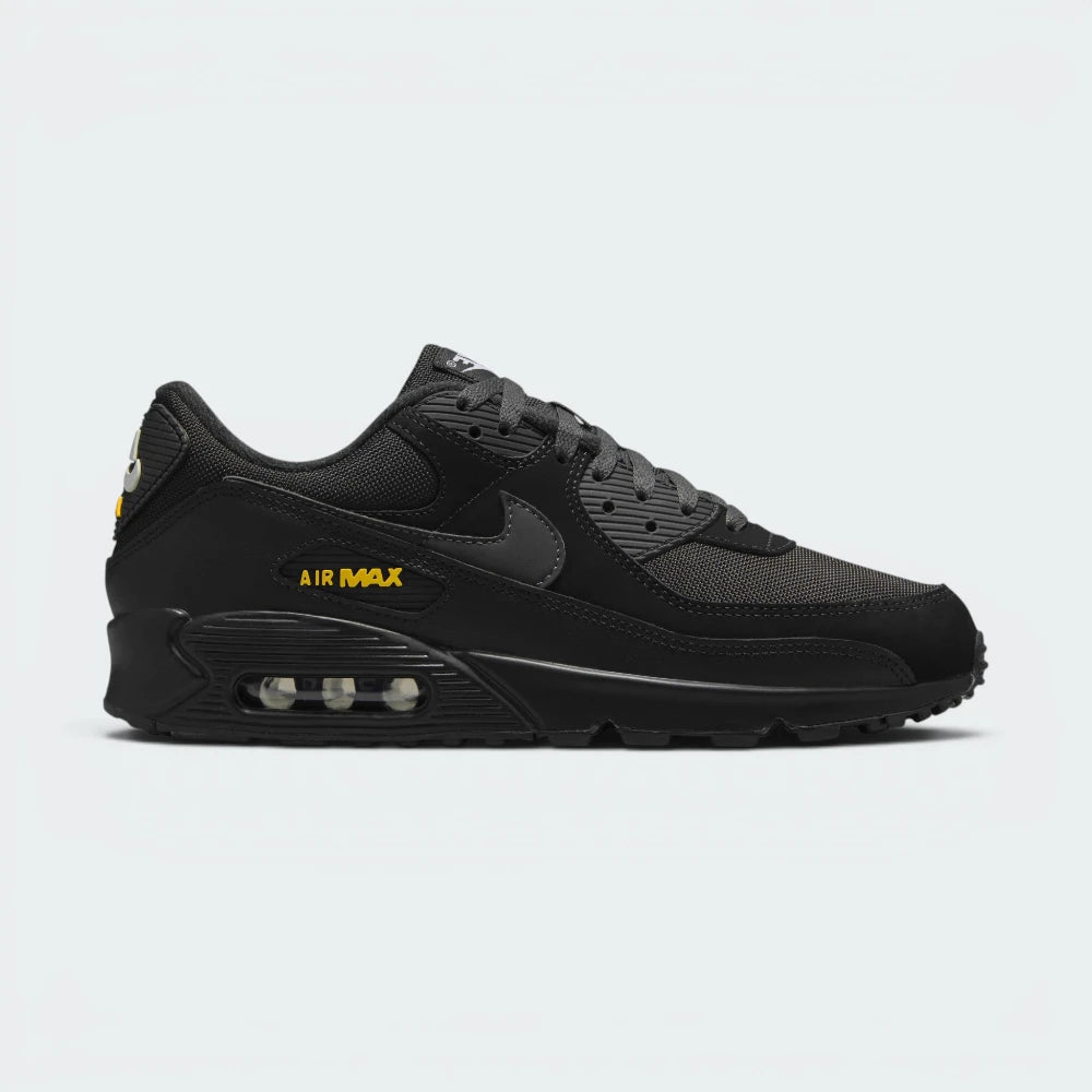 Highlights the high-velocity sweep of the crisp White Nike Swoosh, showing the professional, layered texture of the Black and Anthracite panels resting above the bold University Gold Max Air cassette window frame. Main image