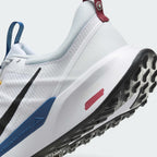 Highlights the "unreal" clean finish where the white foam midsole meets the blue trail clip, painted red trail signpost graphic, and toothy black rubber tread below.